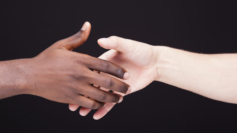African and a caucasian man shaking hands over black background